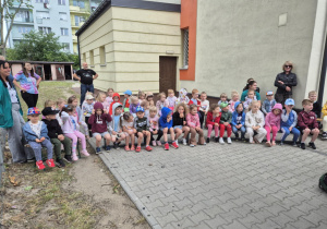 Dzieci siedzą na ławkach na dziedzińcu przedszkola