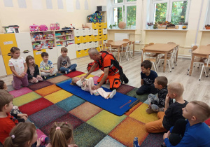 Ratownik uczy dzieci ułożenia osoby poszkodowanej w pozycji bocznej.