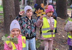 Dzieci pozują do zdjęcia z zebranymi liśćmi.