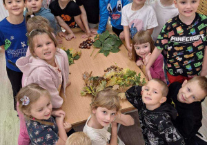 Dzieci pozują do wspólnego zdjęcia z zebranymi darami jesieni.