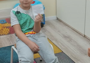 Chłopiec pozuje do zdjęcia. W ręku trzyma logo samochodu.