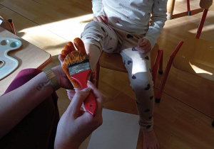 Nauczycielka maluje dziewczynce stopę.
