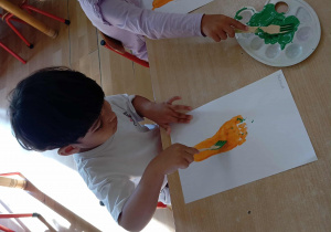Dzieci malują widelcem natkę marchewki.