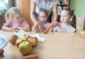 Nauczycielka pomaga dzieciom obierać marchewkę