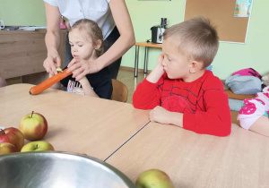 Nauczycielka pomaga dzieciom obierać marchewkę