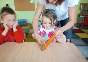 Nauczycielka pomaga dzieciom obierać marchewkę