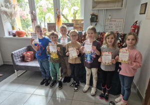 Dzieci pozują do zdjęcia na tle prac konkursowych