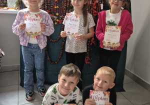 Dzieci pozują do zdjęcia na tle prac konkursowych