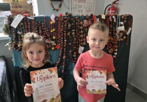 Dzieci pozują do zdjęcia na tle prac konkursowych