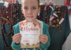 Chłopiec pozuje do zdjęcia na tle prac konkursowych