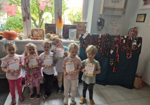 Dzieci pozują do zdjęcia na tle prac konkursowych