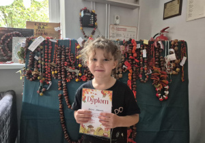 Dziewczynka pozuje do zdjęcia na tle prac konkursowych