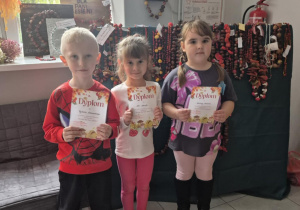 Dzieci pozują do zdjęcia na tle prac konkursowych