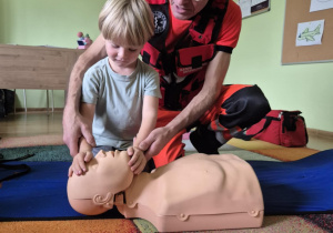 Chłopiec przy pomocy ratownika ćwiczy udzielanie pierwszej pomocy
