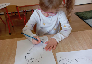 Dziewczynka rysuje po śladzie marchewkę.