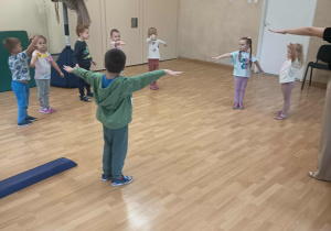 Dzieci stoją w kole z rozłożonymi na boki rękami