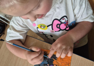 Dziewczynka siedzi przy stoliku, wydrapuje wzorki na kartoniku pokrytym plasteliną