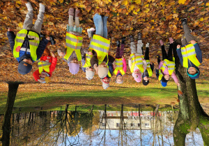 Grupa dzieci podskakując, rozrzuca liście w parku rękoma do góry.