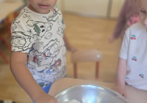 Chłopiec wsypuje mąkę do miski.