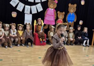 Dziewczynka przebrana za misia stoi z mikrofonem na środku sceny