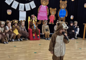 Chłopiec przebrany za misia stoi z mikrofonem na środku sceny