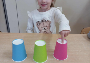 Dziewczynka odgaduje pod którym kubkiem jest piłka.