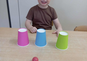 Chłopiec odgaduje pod którym kubkiem jest piłka.