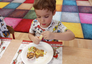 Chłopiec dekoruje pierniki i babeczkę.