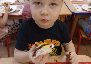 Chłopiec degustuje udekorowana przez siebie babeczkę.