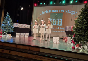 Trzy dziewczynki w strojach aniołków śpiewają na scenie