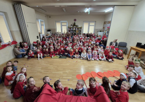 Dzieci z całego przedszkola w świątecznych strojach siedzą na sali gimnastycznej