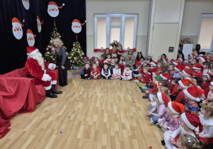 Święty Mikołaj siedzi przed dziećmi w świątecznych strojach
