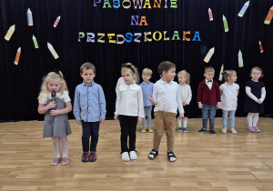 Dzieci stoją na scenie, jedna z dziewczynek mówi do mikrofonu