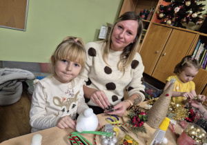 Mama z córką siedzą przy stoliku, robią stroik