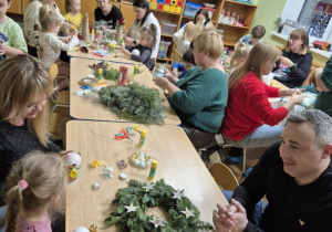 Rodzice z dziećmi siedzą przy stolikach, robią stroiki