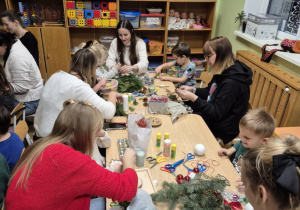 Rodzice z dziećmi siedzą przy stolikach, robią stroiki