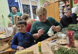 Babcia z wnuczkiem siedzą przy stoliku, robią stroik