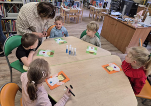 Dzieci siedzą przy stolikach, wykonują pracę plastyczną