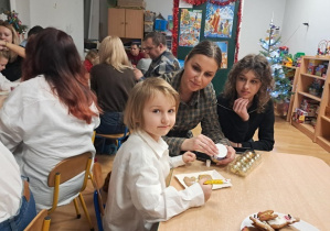 Dziewczynka z rodziną dekoruje pierniczki.