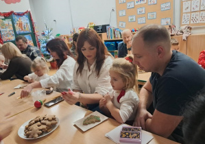 Dziewczynka z rodzicami ozdabia pierniczki.