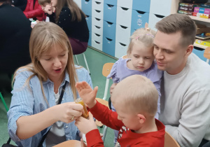 Rodzice z dziećmi siedzą przy stolikach, ozdabiają bombki.