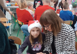 Mama z córką siedzą przy stoliku, ozdabiają bombkę.