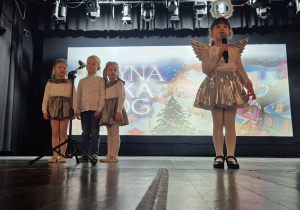 Hania na scenie KDK prezentuje pastorałkę "Aniołek maleńki jak wróbelek". Towarzyszy jej chórek w składzie: Hania K., Franek i Hania Ł.