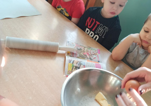 dzieci patrzą jak nauczyciel dodaje jajka do ciasta