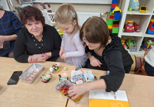 dziewczynka z babcią dekoruje babeczkę owocami