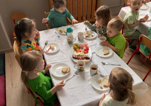 Dzieci siedzą przy stole i spożywają posiłek.