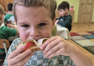 Chłopczyc ze smakiem zjada kanapkę z wędliną i papryką.