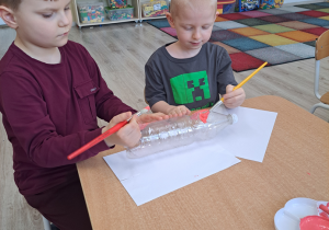 Dzieci malują farbami plastikowe butelki.