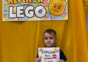 Tymek pozuje z dyplomem mistrza budowania