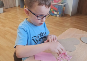 Chłopiec wykleja wydzieranką serduszko.